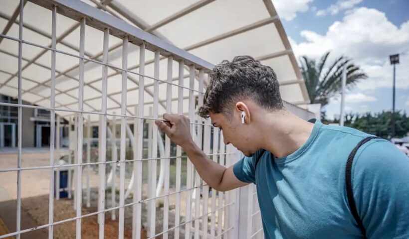 Jovem agarra grade de escola fechada antes de ele conseguir chegar para a prova do Enem. Prazo para solicitar reaplicação do Enem 2023 começa nesta segunda