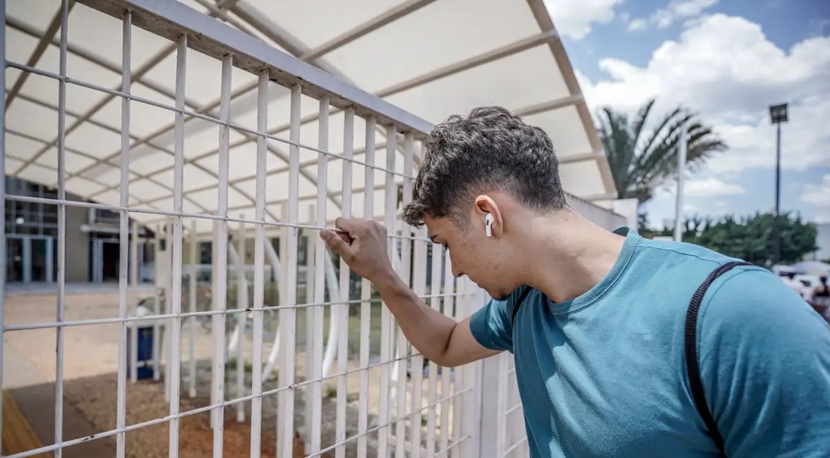 Jovem agarra grade de escola fechada antes de ele conseguir chegar para a prova do Enem. Prazo para solicitar reaplicação do Enem 2023 começa nesta segunda