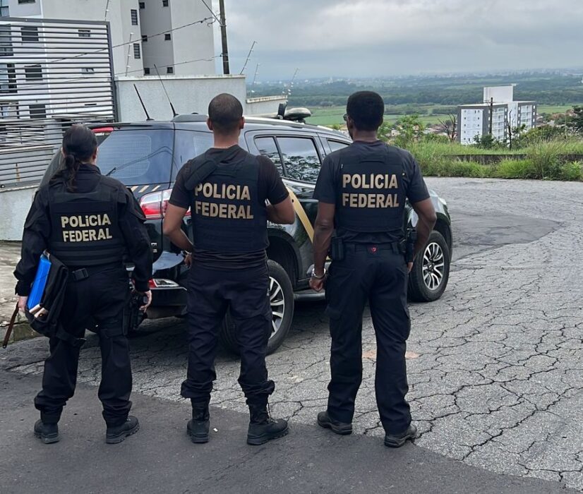 Três policiais federais de costas observam local alvo de operação. Polícia Federal cumpre mandado de busca e apreensão por suposto "caixa 2" eleitoral em Aparecida