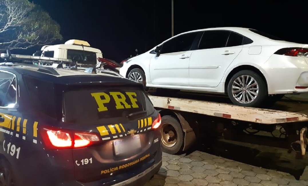 Foto traseira de viatura da PRF ao laco de veículo branco sendo guinchado. Casal é preso pela PRF em Minas Gerais após tentativa de homicídio de empresário em Guaratinguetá
