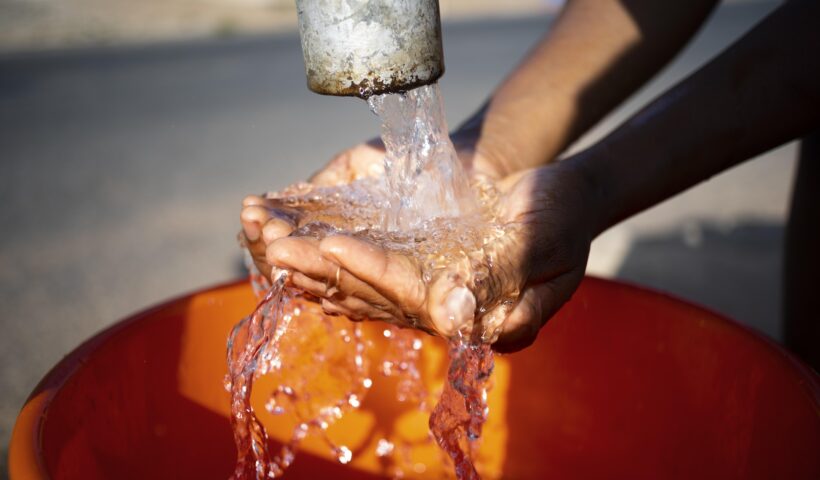 mãos femininas molhando as mãos em tubulação de água que enche balde. Abastecimento de água em Lavrinhas está em recuperação após danos provocados por chuva, diz Sabesp