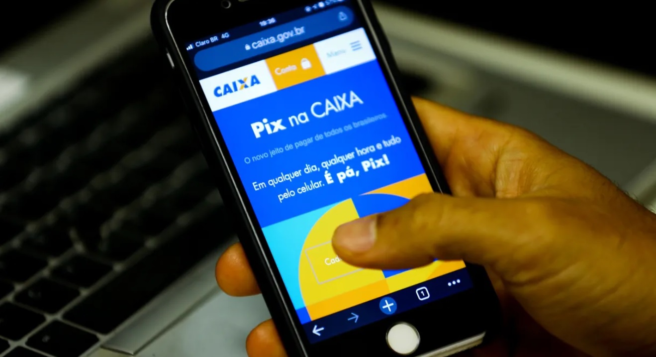 Mãos segurando celular com tela do app da Caixa.