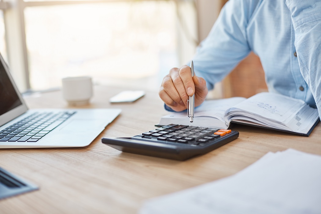 Feche os detalhes do contador sério profissional sentado em um escritório leve, verificando os lucros financeiros da empresa na calculadora, anotando os resultados no caderno. Conceito de negócios. Saiba como declarar o IR 2025 e evite a malha fina
