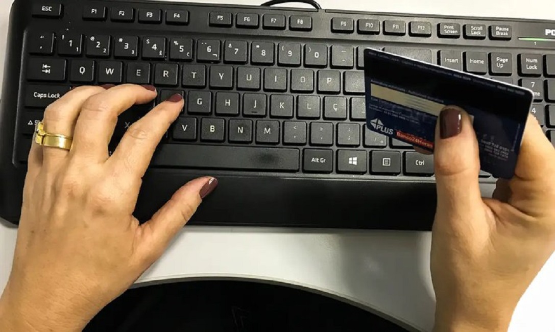 mãos segurando cartão de credito apoiadas em teclado de computador. Novo teto de juros para faturas de cartão de crédito tem início na quarta-feira (3)