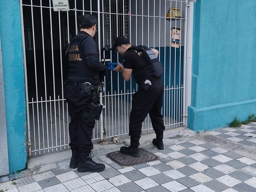Dois agentes da PH com alicate e arrombando portão de ferro de casa de suspeito. Homem é preso por se passar por menina e extorquir fotos íntimas de menores, em Jacareí