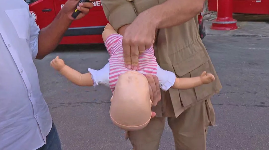 Bombeiro simula apertar com dois os dedos o peito de um boneco, entre os mamilos, para desengasgar um bebê