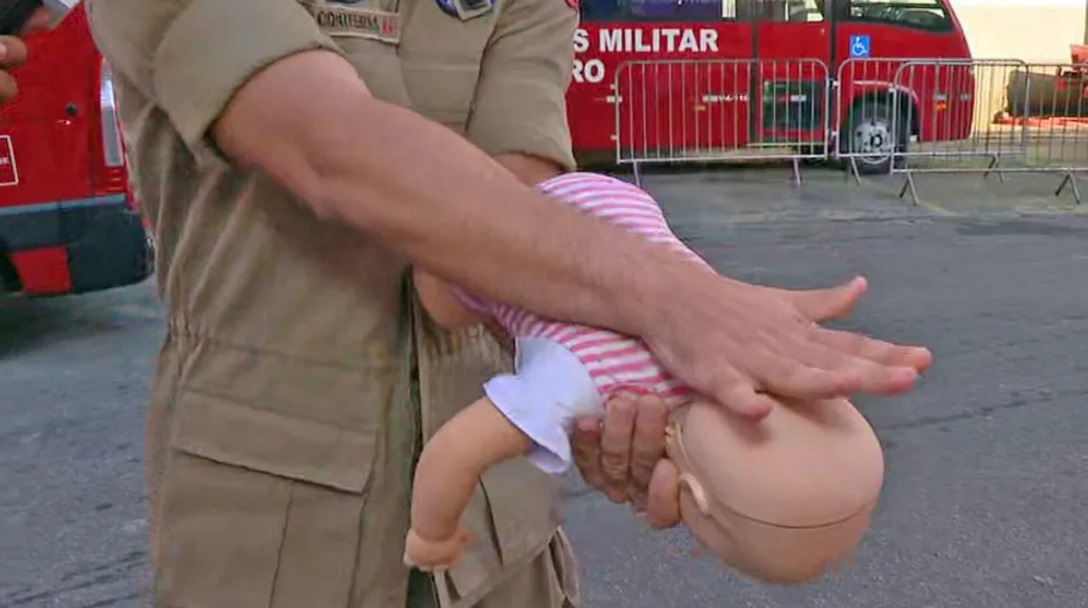 Bombeiro simula dar tapas nas costas de um boneco, segurando-o pelo antebraço, para desengasgar um bebê