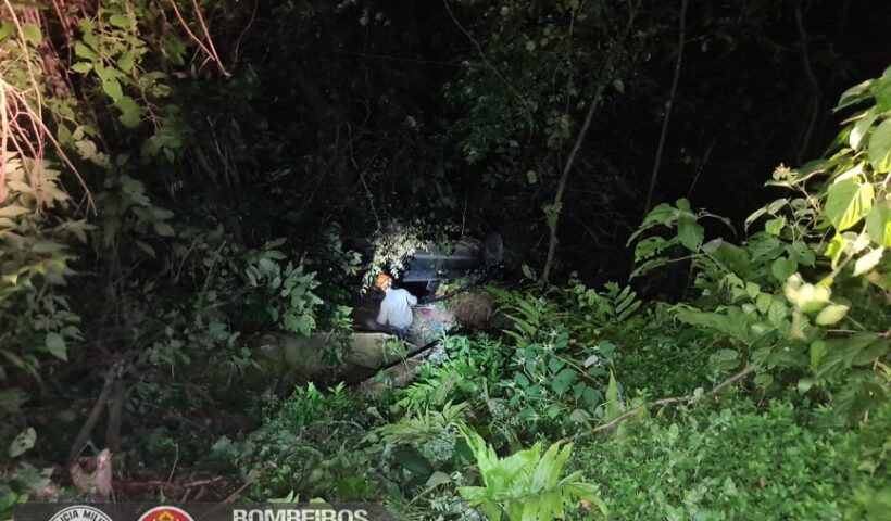 Vista de ribanceira onde bombeiro se aproxima de veículo acidentado. Bombeiros resgatam ocupantes de veículo que caiu em ribanceira, na Rio-Santos, em São Sebastião