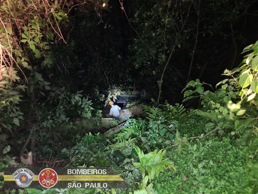 Vista de ribanceira onde bombeiro se aproxima de veículo acidentado. Bombeiros resgatam ocupantes de veículo que caiu em ribanceira, na Rio-Santos, em São Sebastião