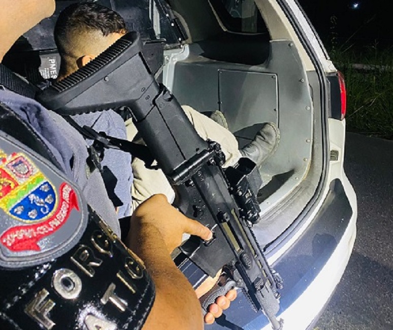 PM com fuzil acompanha suspeito algemado sair de viatura policial