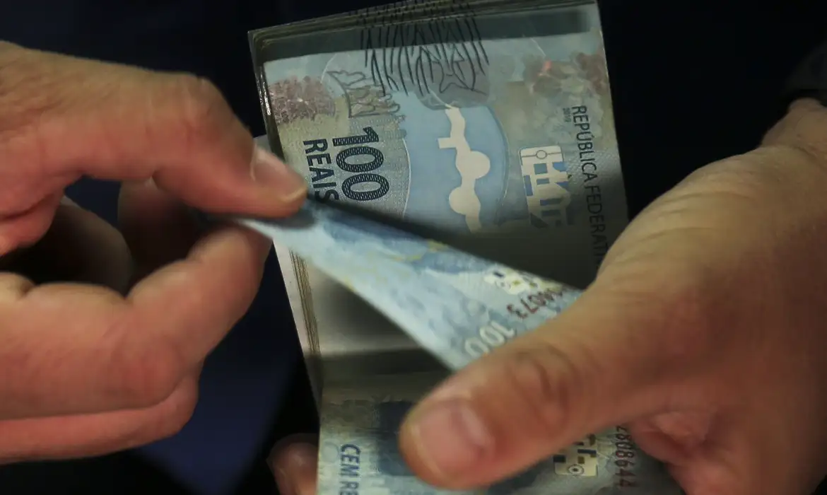 mãos contando dinheiro. INSS paga segunda parcela do 13º a quem recebe acima do mínimo