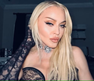 Foto que ilustra o Show da Madonna, que acontecerá no Rio de Janeiro no próximo sábado; na foto a artista aparece com o cabelo loiro, uma roupa preta mostrando os ombros, maquiagem preta, e olhando para a câmera.