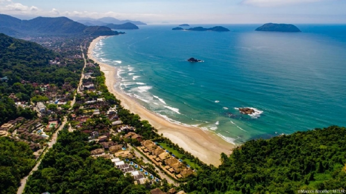 Vista aérea da Praia de Juquehy, com o mar ao fundo, o céu em cima, faixa de areia e árvores ao redor, ilustrando as buscas pelo adolescente que desapareceu em São Sebastião, realizadas pelo GBMAR.