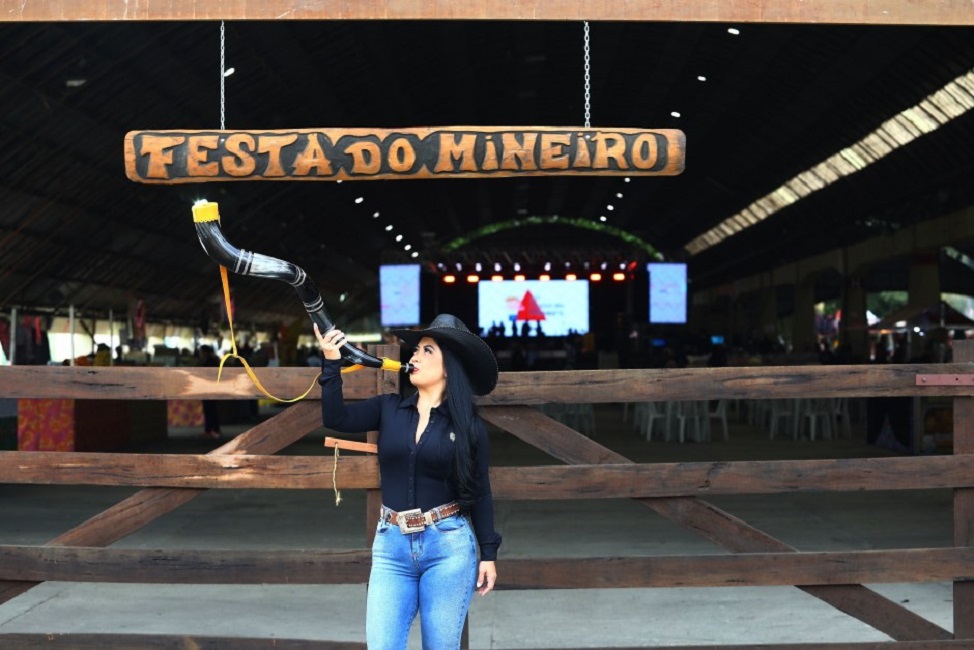 Mulher tocando um berrante, em frente à fachada da Festa do Mineiro, que acontece em São Jose dos Campos anualmente no Parque da Cidade.