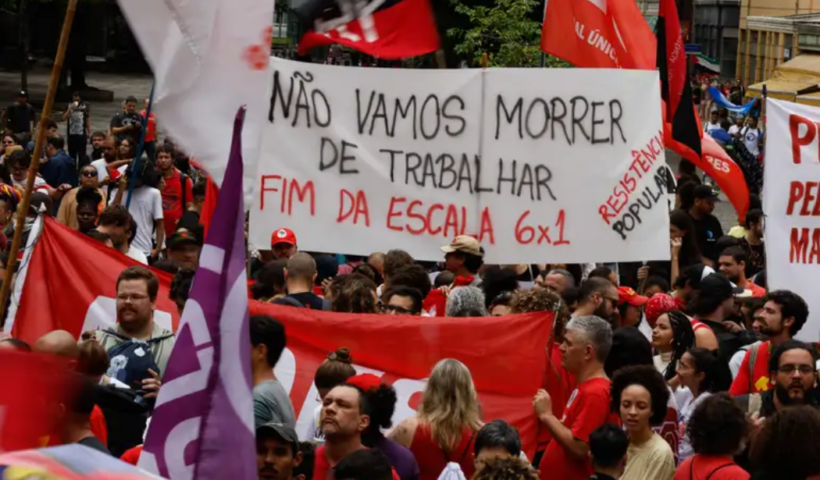 Protesto com diversas pessoas de vermelho e um cartaz em destaque escrito: não vamos morrer de trabalhar fim da escala 6x1 resistência popular