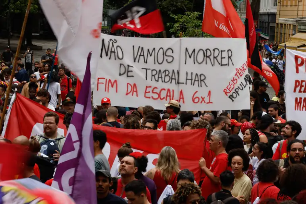 Protesto com diversas pessoas de vermelho e um cartaz em destaque escrito: não vamos morrer de trabalhar fim da escala 6x1 resistência popular