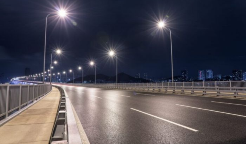Rodovia com diversas luzes bem fortes, sem carros, mostrando cidade ao fundo