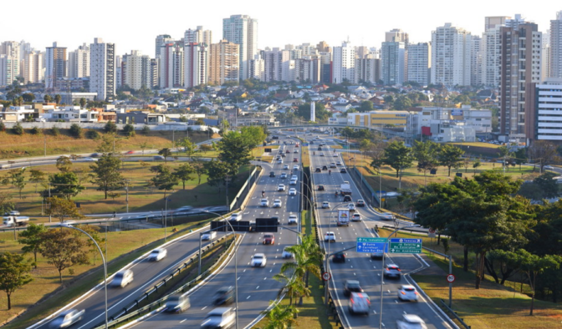 Visão do Anel Viário de São José dos Campos com diversos carros passando, prédios ao fundo