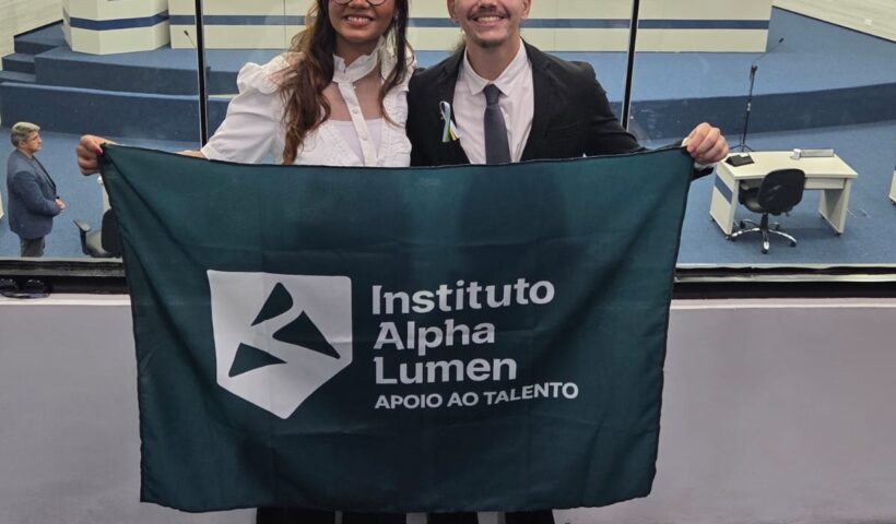 dois alunos segurando a bandeira da escola Alpha Lumen, no plenário da Câmare de SJC, reforçando ações para os cuidados com o autismo