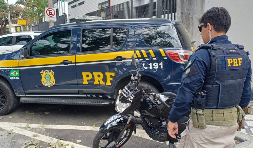 agente da PRF ao lado de moto apreendida e próximo à viatura policial