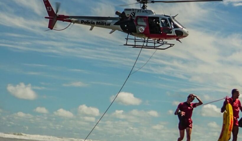 Helicóptero sobrevoa próximo à praia com 2 salva-vidas correndo para a areia