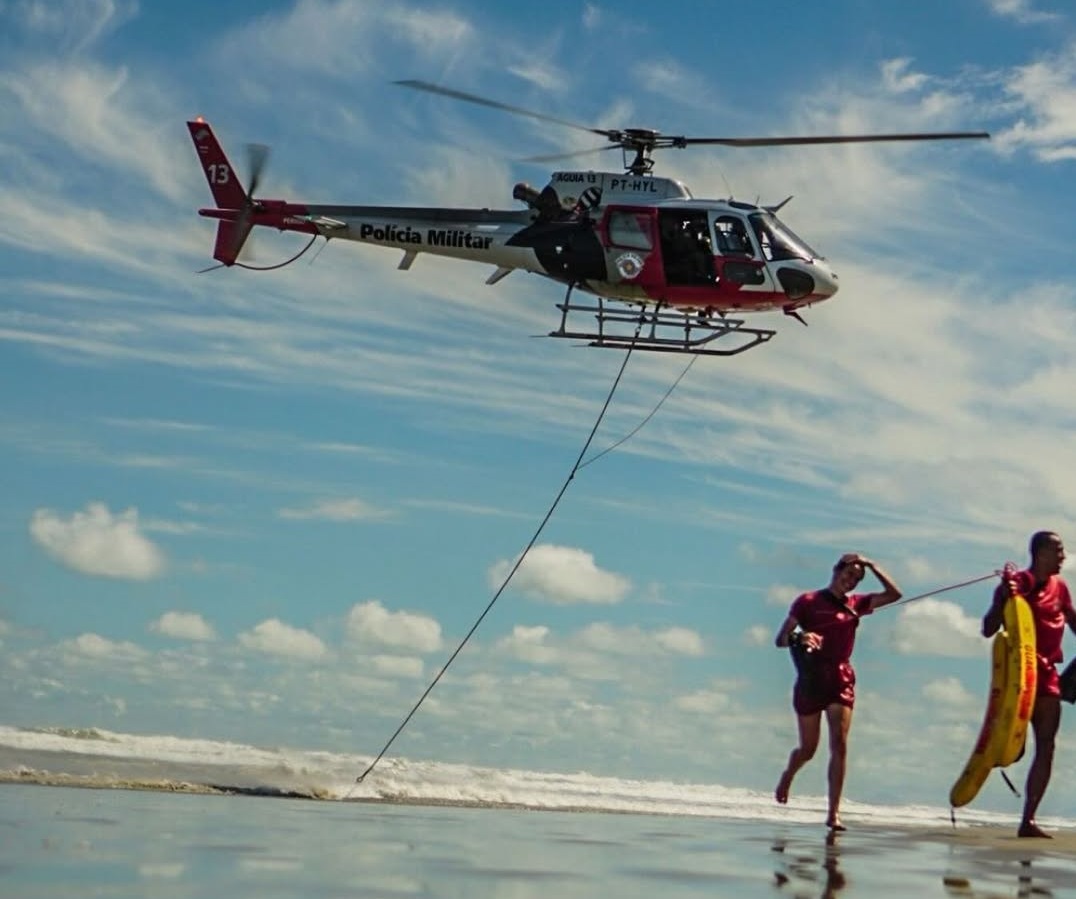 Helicóptero sobrevoa próximo à praia com 2 salva-vidas correndo para a areia